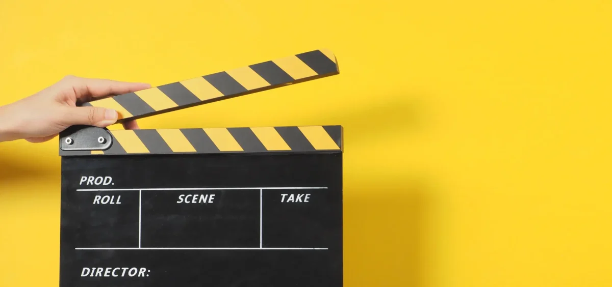 Hand is holding black clapper board or movie slate.It is used in video production and movies, film industry on yellow background.